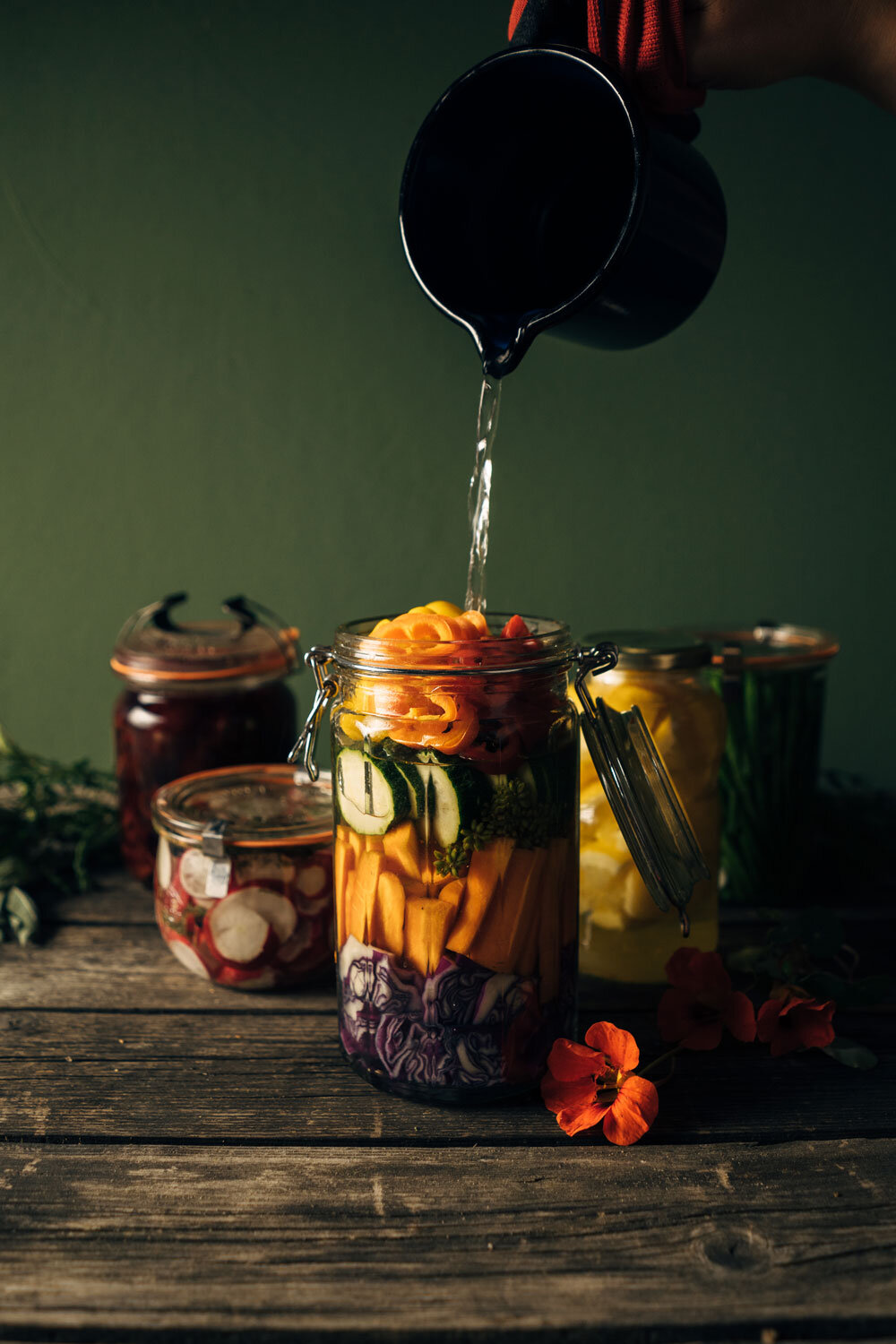 Preserving vegetables: liquid being poured into a clip-top jar of colourful chopped vegetables