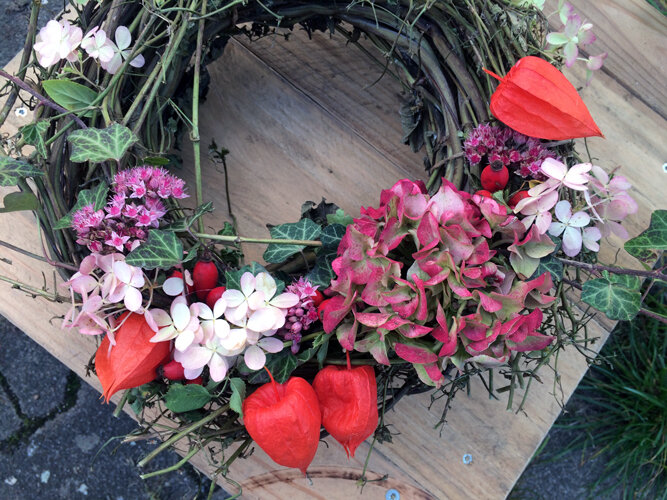 Handmade autumn wreath with pink flowers, orange-red Chinese lanterns and green leaves on a board