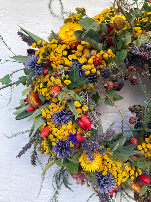 Close-up of a finished autumn wreath with yellow and blue flowers, red rosehips and dark berries