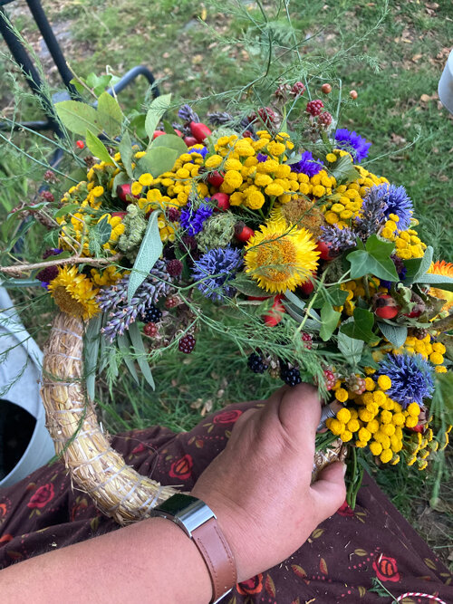 Half-finished autumn wreath of yellow and blue flowers, grasses and berries on a straw base