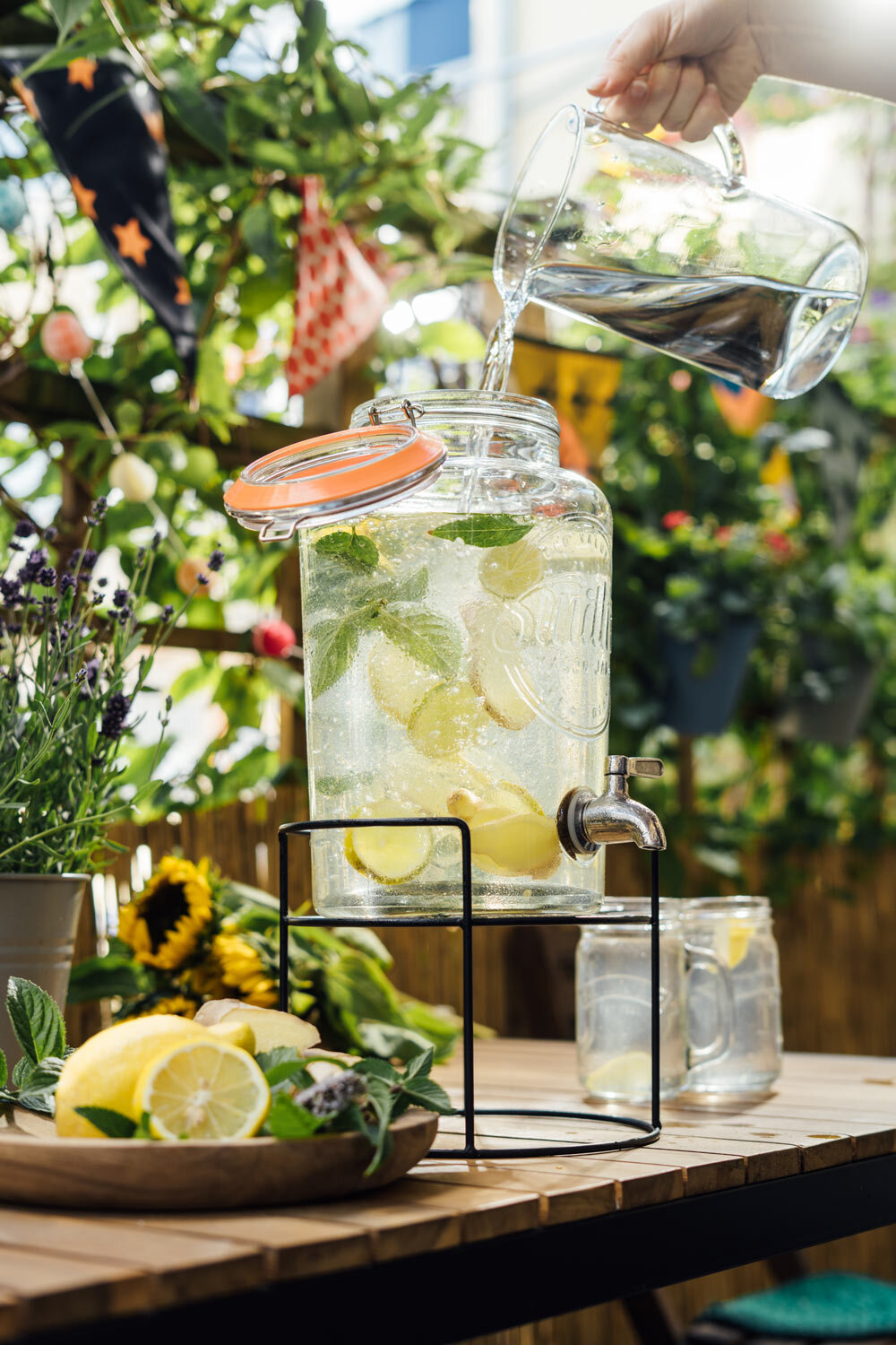 Water poured into a drinks dispenser with lemon and mint, homemade lemonade on a balcony