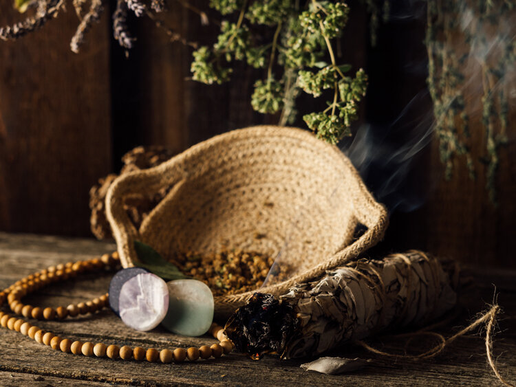 Smouldering sage smudge stick beside a smudge bowl, stones and a wooden bead necklace