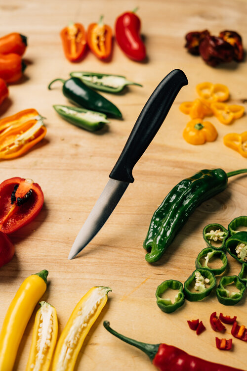 Sliced chillies in red, yellow, orange and green with a knife on a wooden board